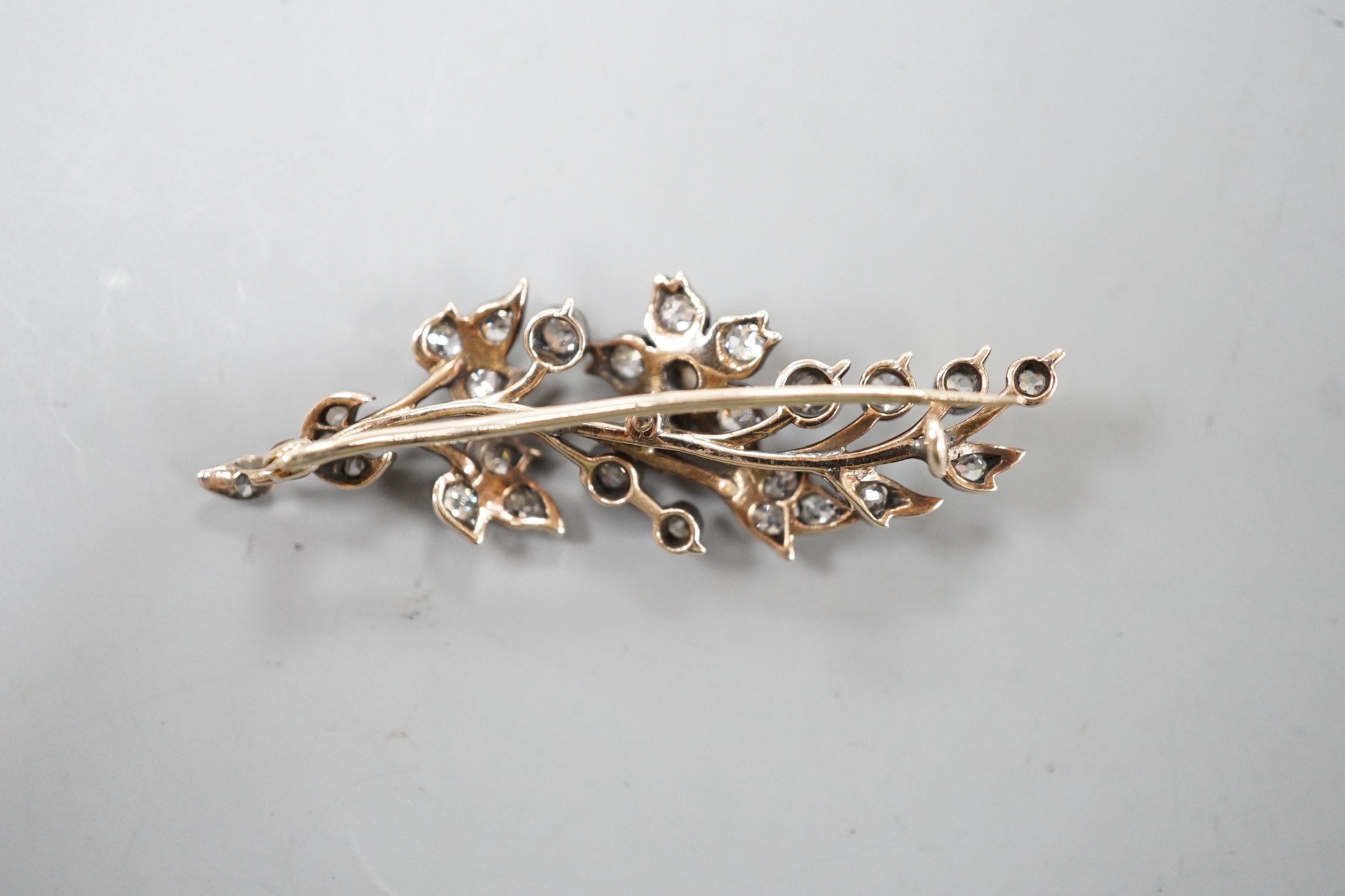 A yellow metal and diamond cluster set foliate spray brooch, 47mm, gross weight 4.5 grams.